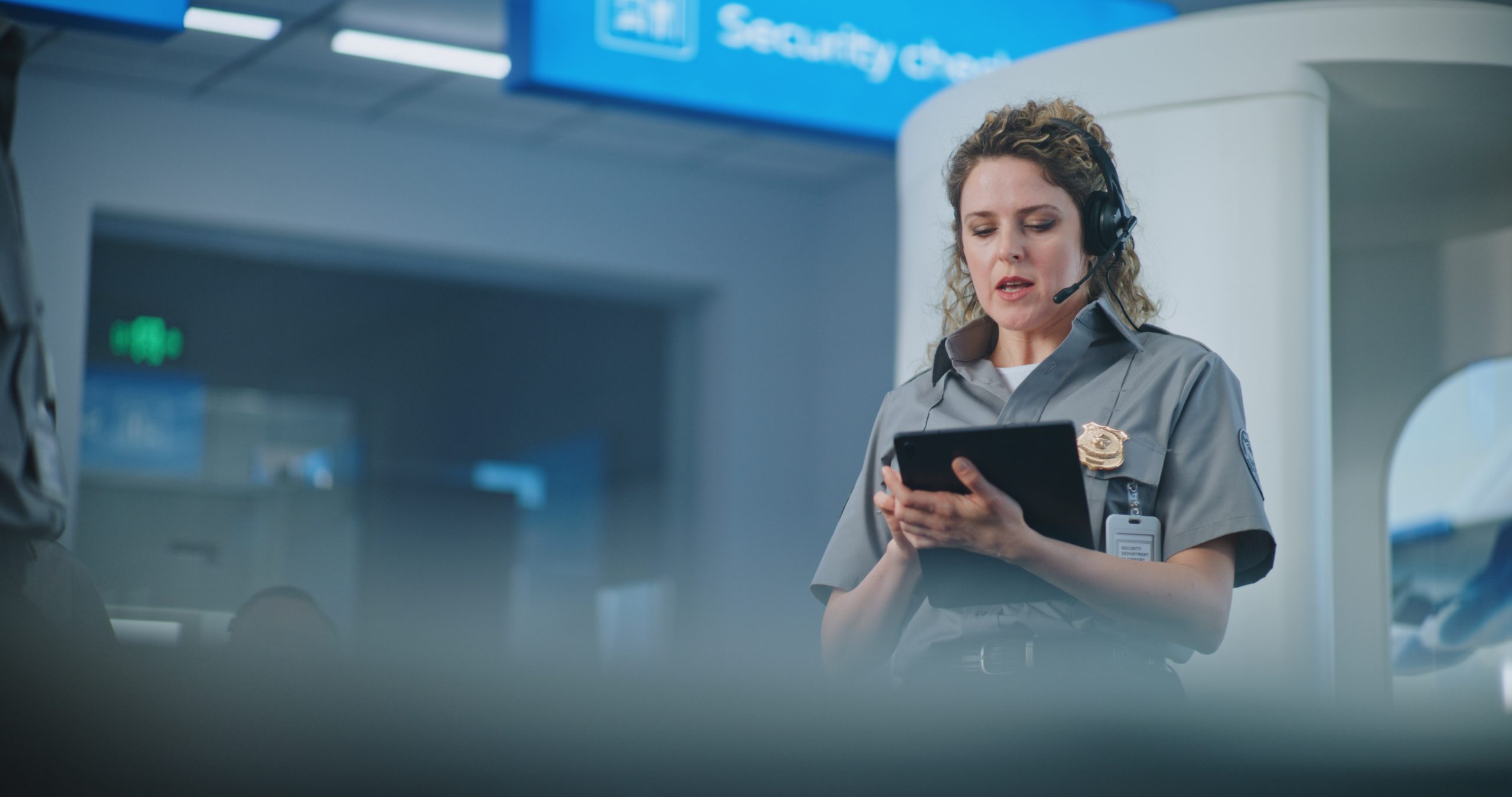 Customs officer in gray uniform using tablet and headset at airport security checkpoint