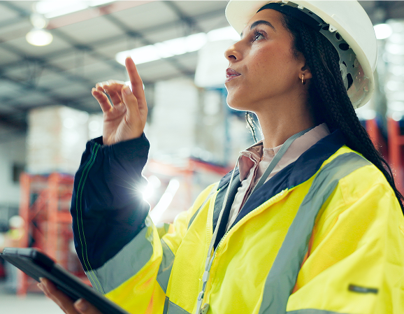 Female logistics professional in high-visibility vest using a tablet in a warehouse