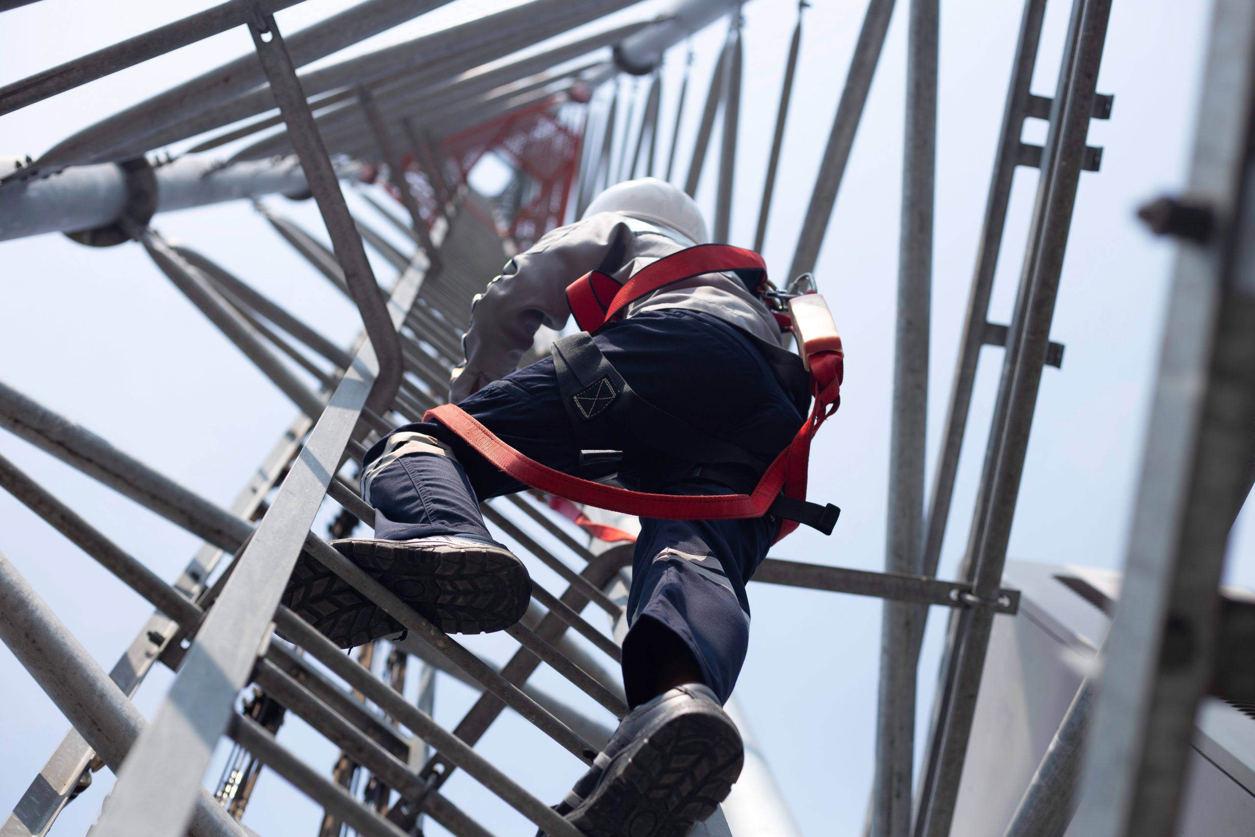 Telecommunications technician climbing a cell tower during network infrastructure deployment.
