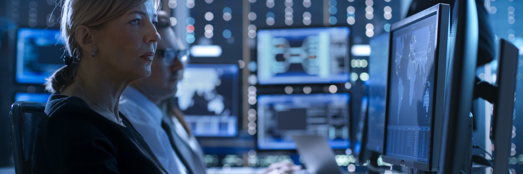 Defence and security personnel monitoring mission-critical digital systems and operational data on multiple screens.