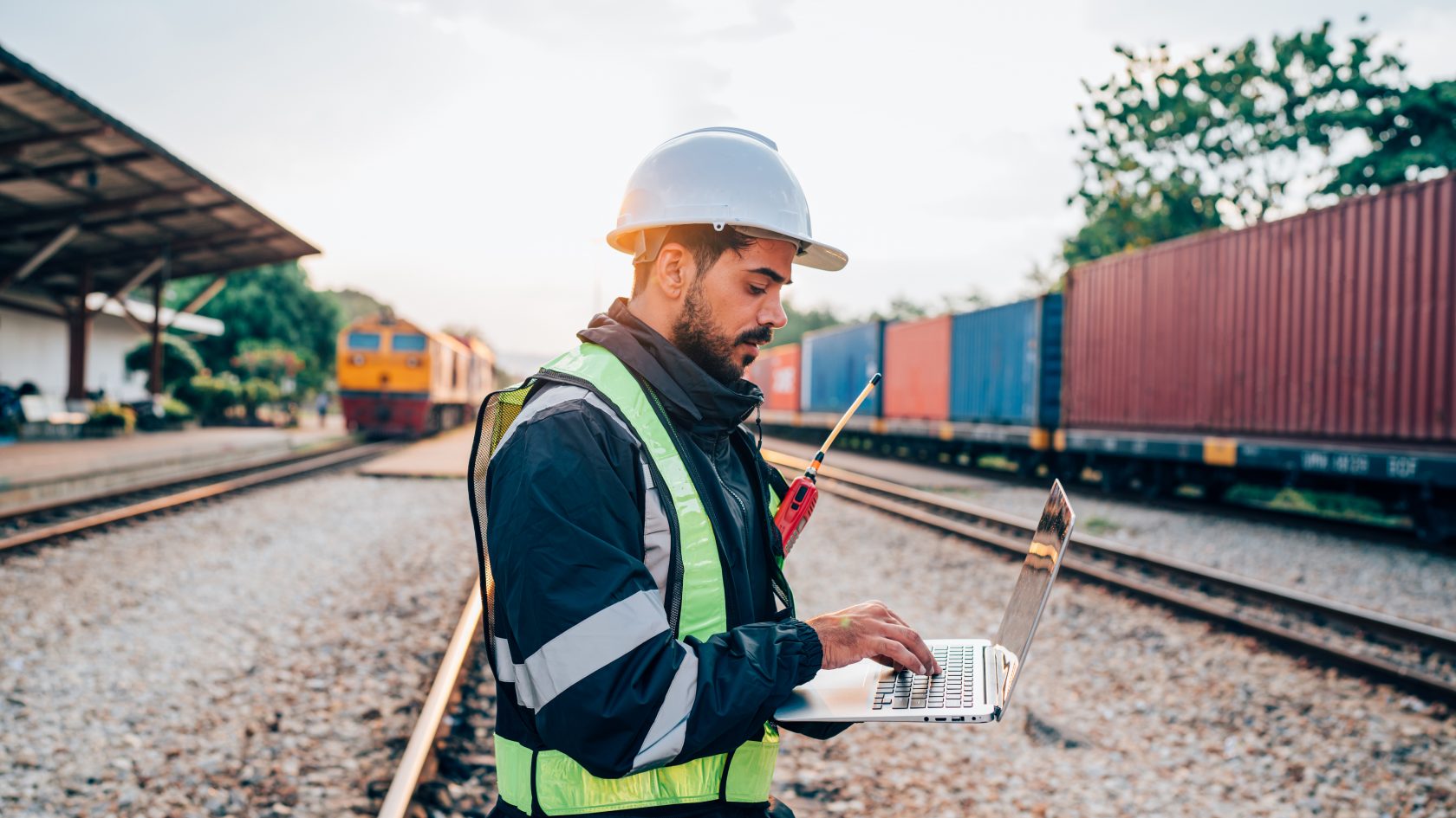 Railway worker using a laptop beside railway tracks to monitor and manage digital rail network operations.
