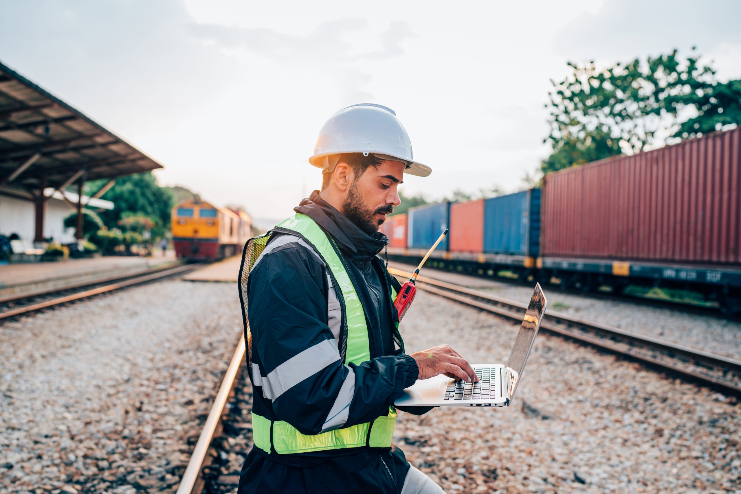 Railway worker using a laptop beside railway tracks to monitor and manage digital rail network operations.