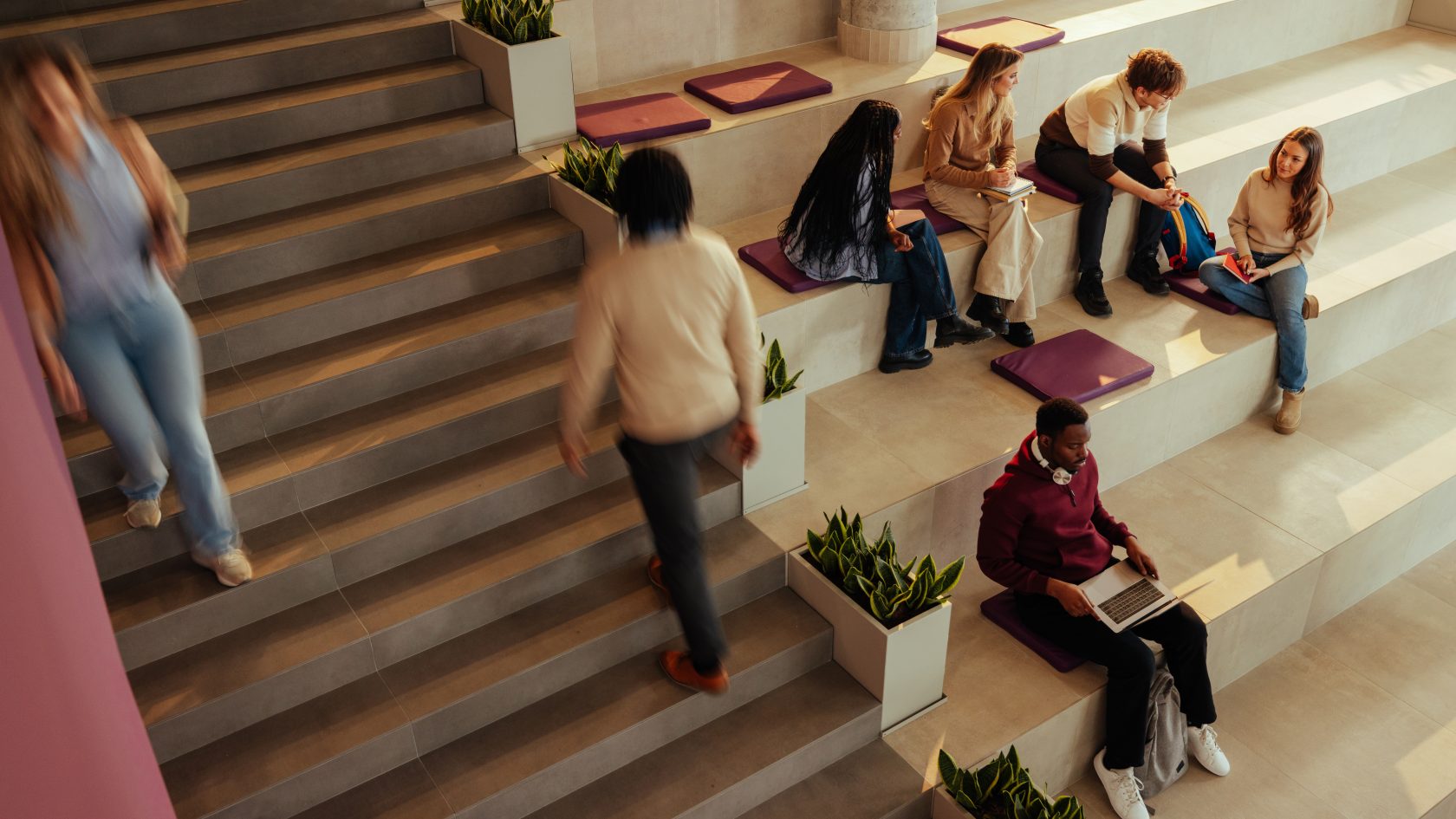 Students and staff using laptops, mobile devices and communal spaces in a modern university campus building.
